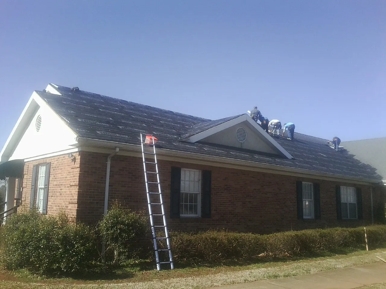 Crew tearing shingles off a brick ranch roof with a ladder set — Emergency Roof Repair work by our crew in Glen Arm