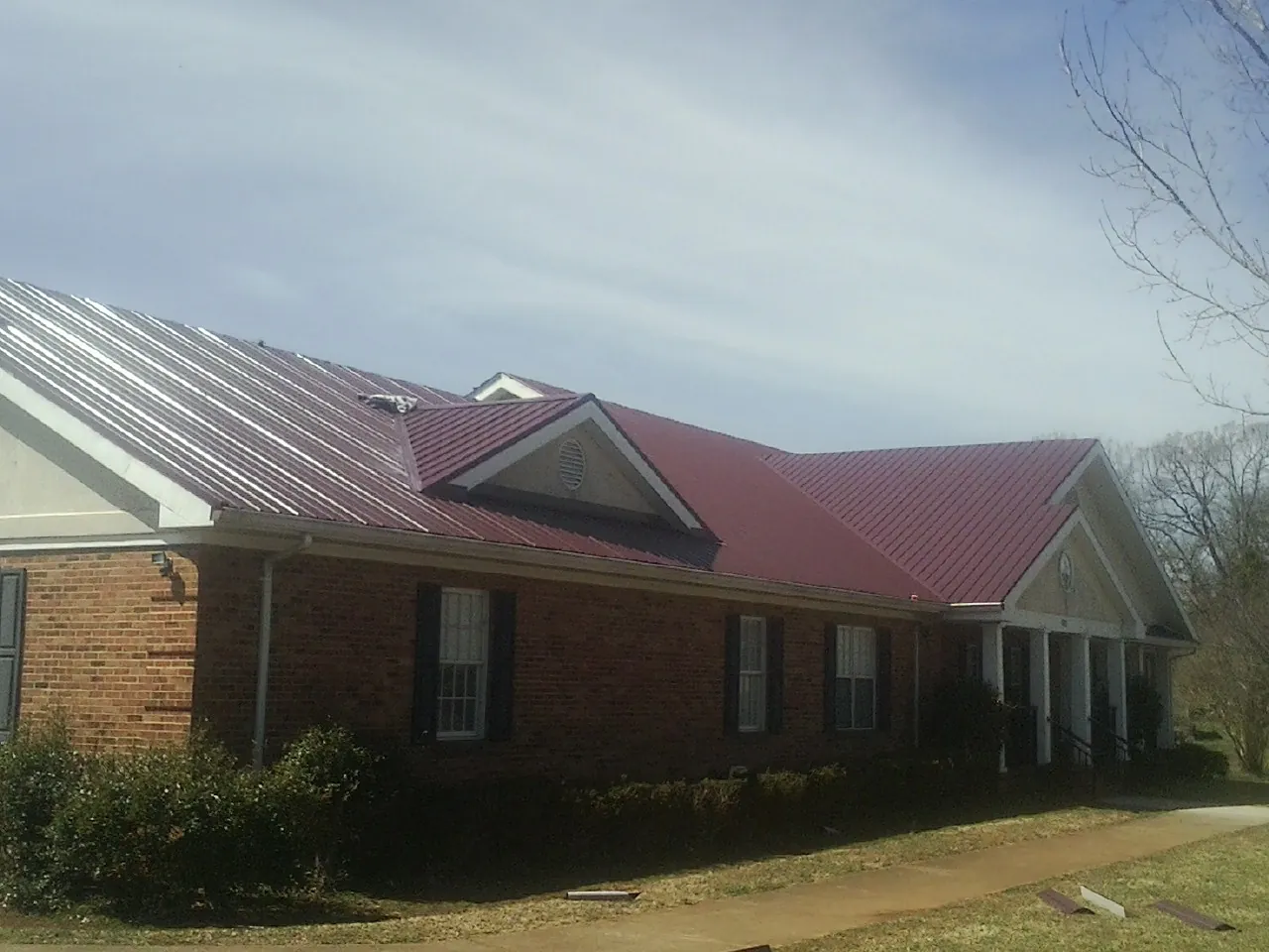 Red metal roof with gabled entries on a long brick building, from a Hail Damage Roof Repair job in Glen Arm