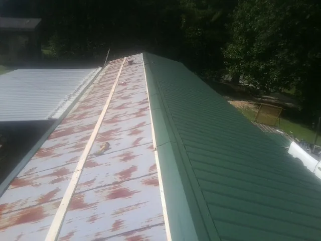 Old rusted panels beside newly installed green metal roofing — Wind Damage Roof Repair by Roofing Brothers in Glen Arm