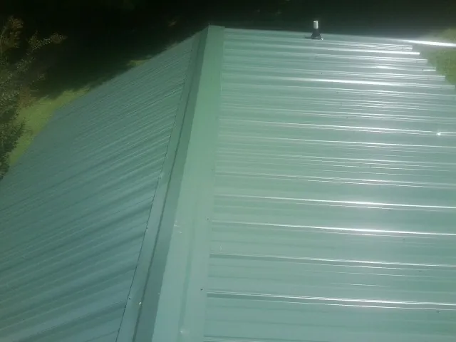 New green metal panels meeting at the ridge of a roof — Flat Roof Repair work by our crew in Glen Arm