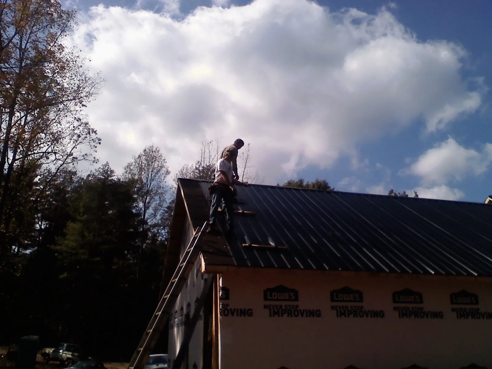 Roofer fastening dark metal panels high against a cloudy sky, from a Roof Inspection job in Glen Arm